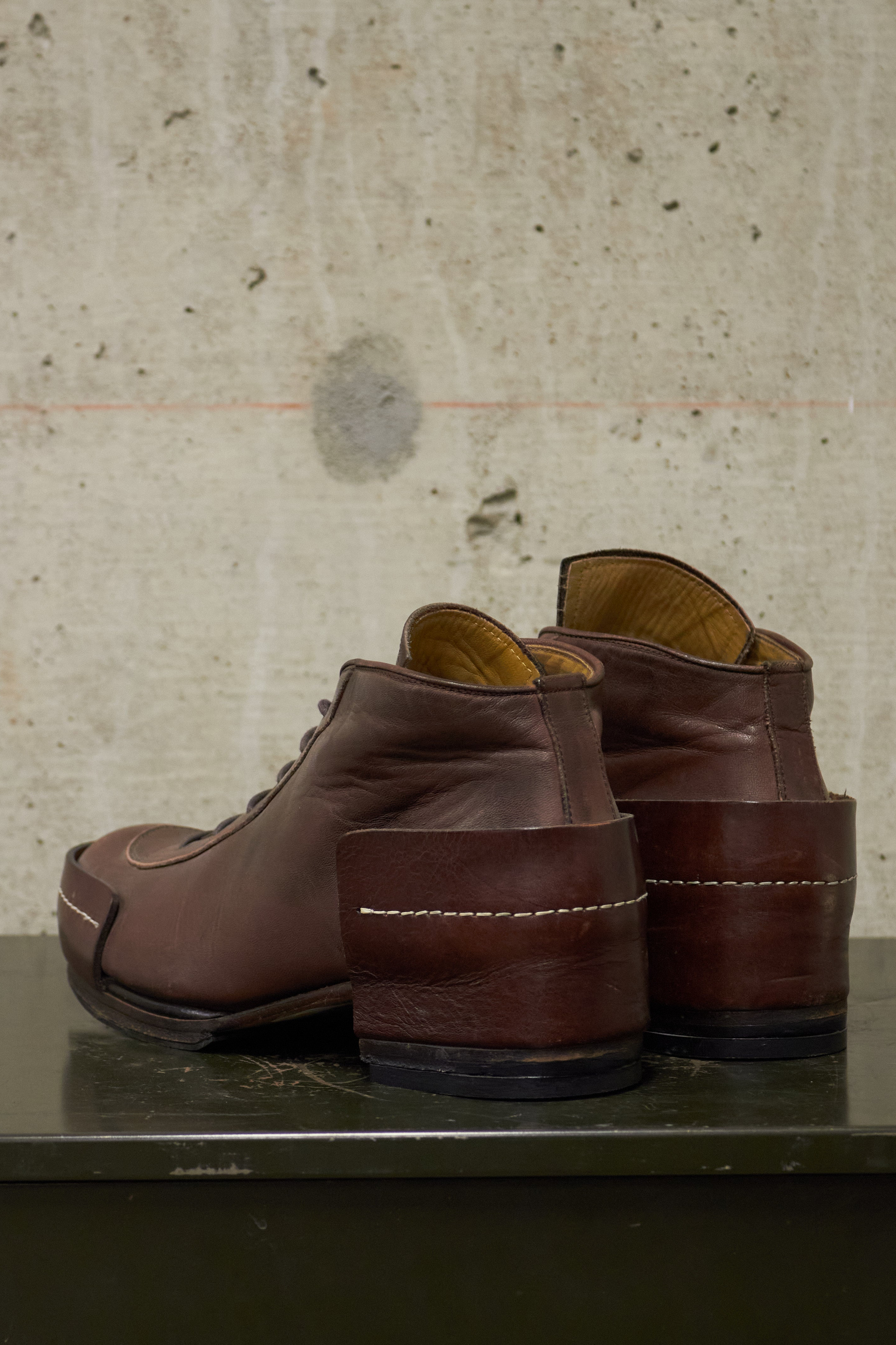 Pair of brown leather shoes on a metallic surface with a textured beige wall background
