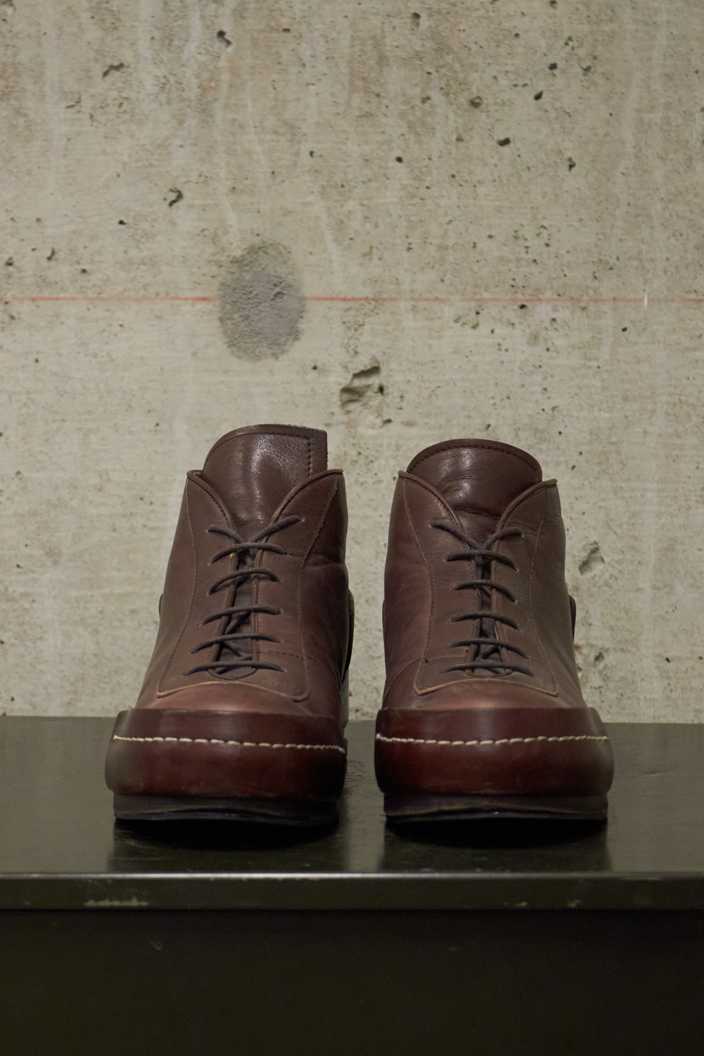 Pair of brown leather boots on a concrete surface with a textured wall background
