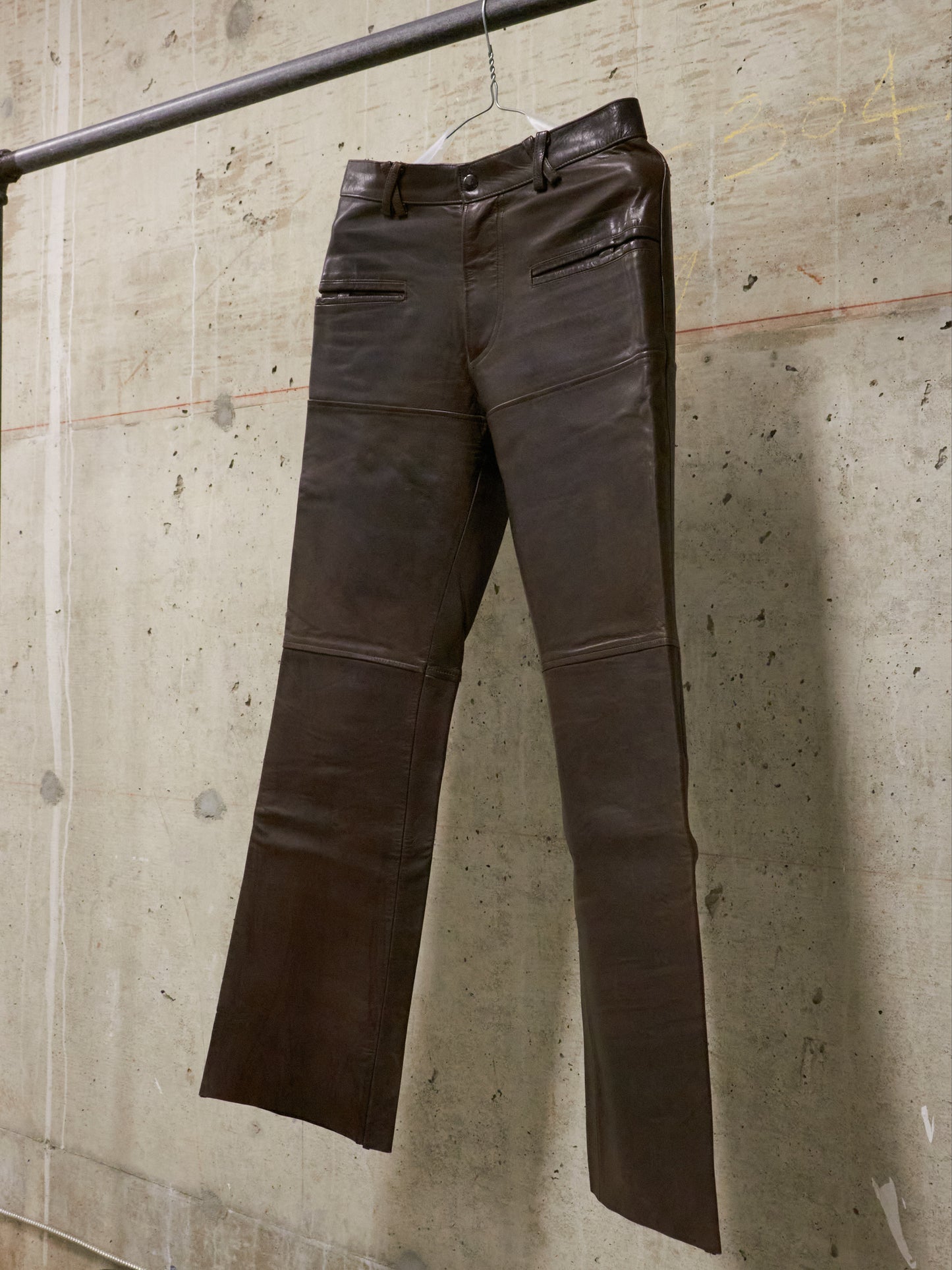 Brown leather pants hanging against a textured concrete wall.
