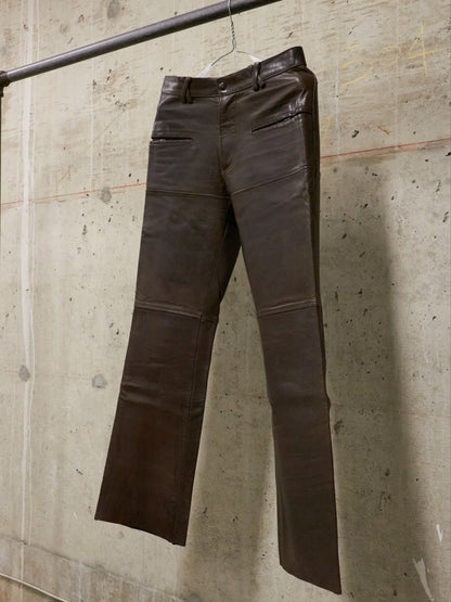 Brown leather pants hanging against a textured concrete wall.
