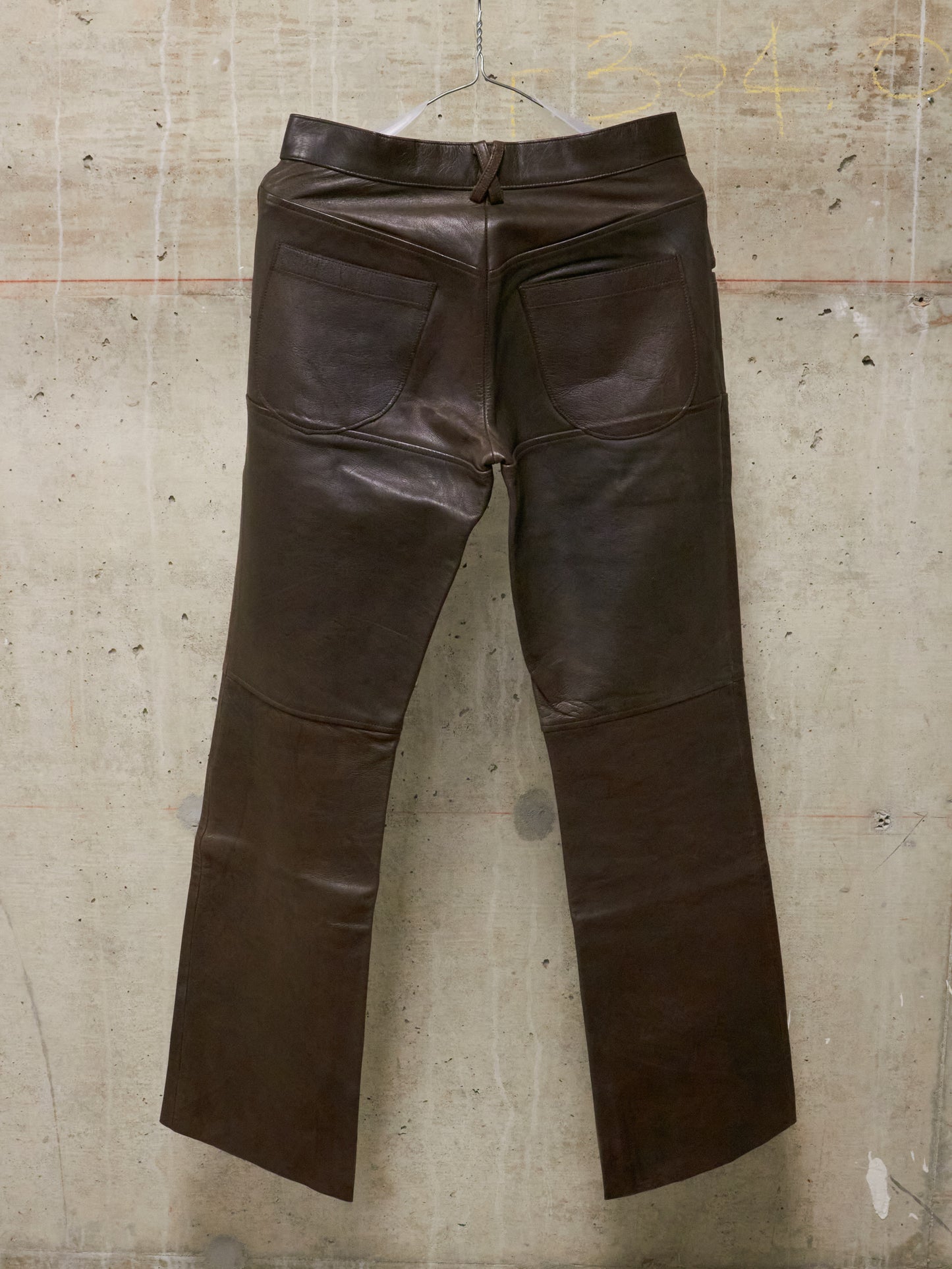 Brown leather pants hanging against a textured wall.