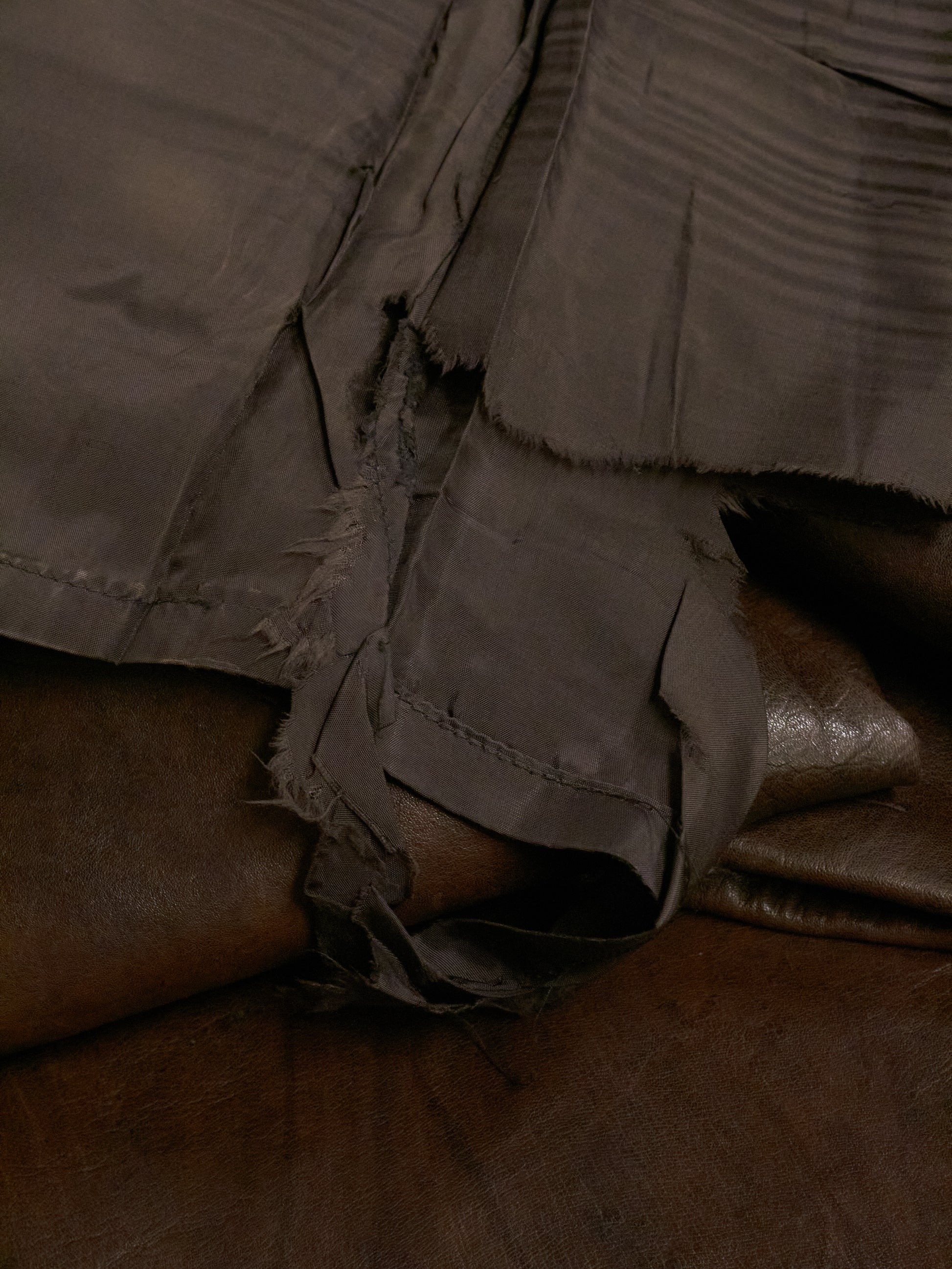 Close-up of a brown leather jacket with frayed edges on a dark surface