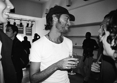 Photo of Martin Margiela founder of Maison Martin Margiela at a dinner party holding a glass, famous fashion designer 