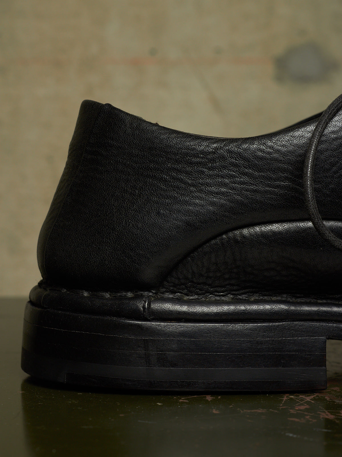 Close-up of a black leather loafer with a chunky black sole, showing the textured grain and stitching details.