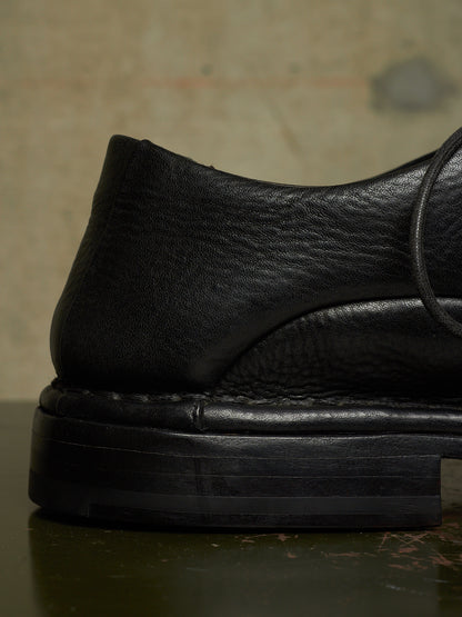 Close-up of a black leather loafer with a chunky black sole, showing the textured grain and stitching details.