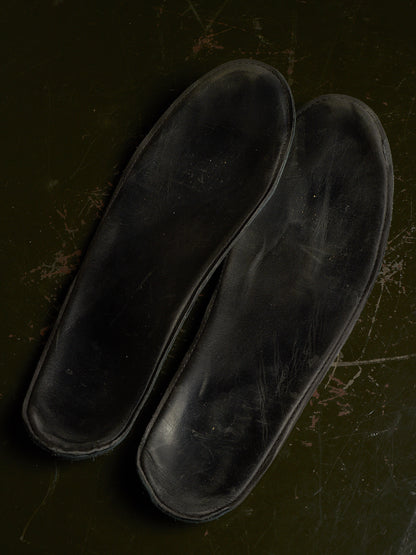 A pair of black shoe insoles photographed from above on a dark olive-green textured surface.