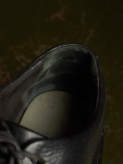Close-up of the opening of a black leather shoe, showing the interior lining and a light-colored footbed, set against a dark, moody background.