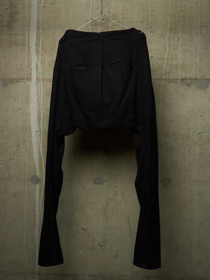 Black high-waisted cropped pants with a dramatic split leg design, hanging on a wire hanger against a textured concrete wall.