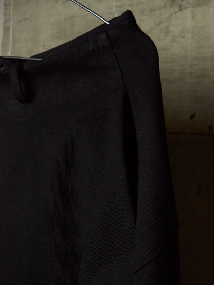 A close-up of a black textured garment, likely a jacket or coat, hanging on a metal hanger against a warm, textured concrete wall.