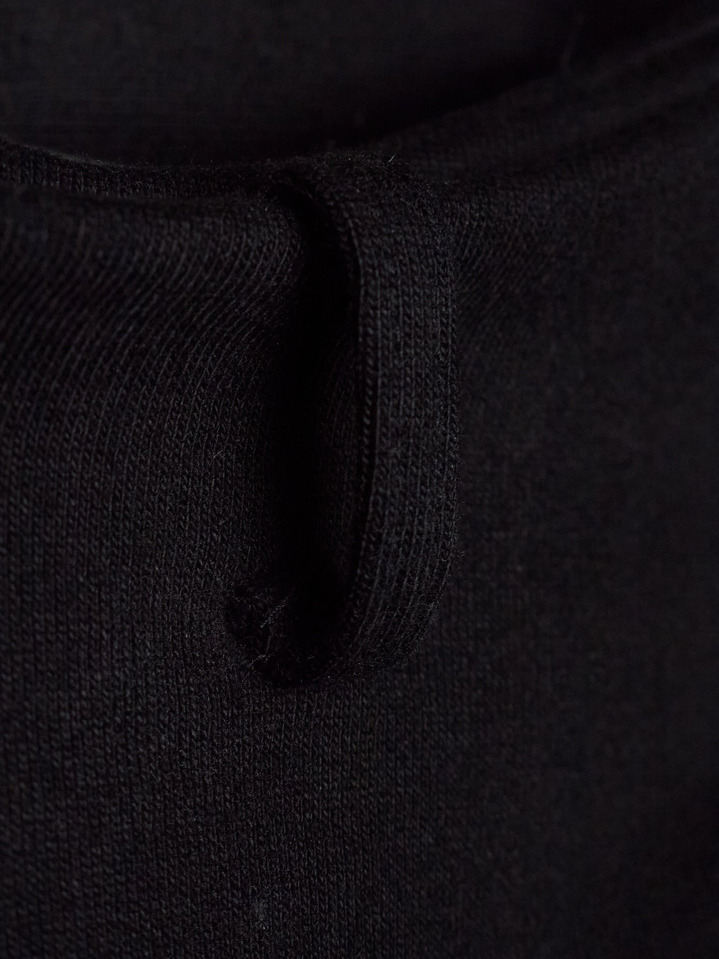 Close-up detail of a black knit garment showing the ribbed texture and a small loop detail.