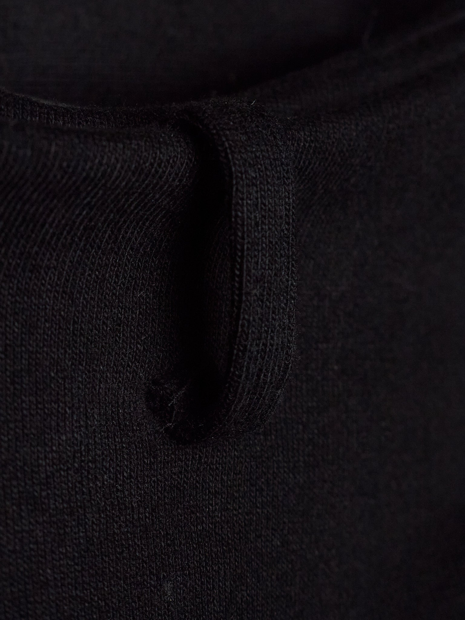 Close-up detail of a black knit garment showing the ribbed texture and a small loop detail.