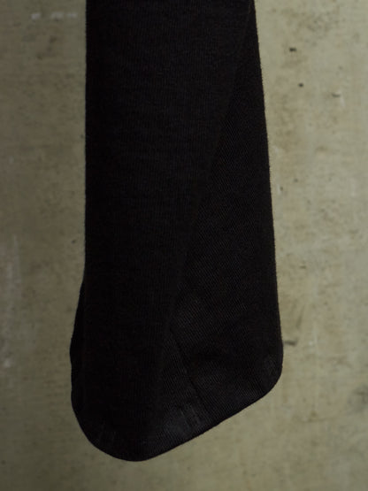 A close-up of a black textured fabric item, possibly a sleeve or pouch, shown against a neutral concrete background.
