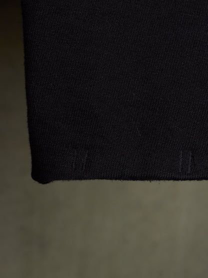 Close-up of a black knit fabric cuff or sleeve hem against a neutral gray background.