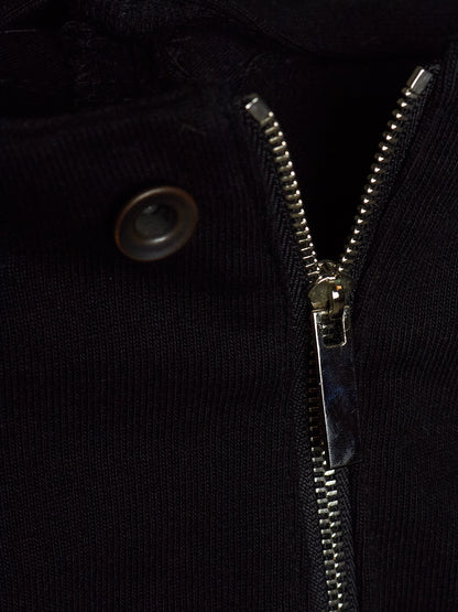 Close-up detail of a black ribbed knit garment featuring a silver metal zipper and a dark metal snap button.
