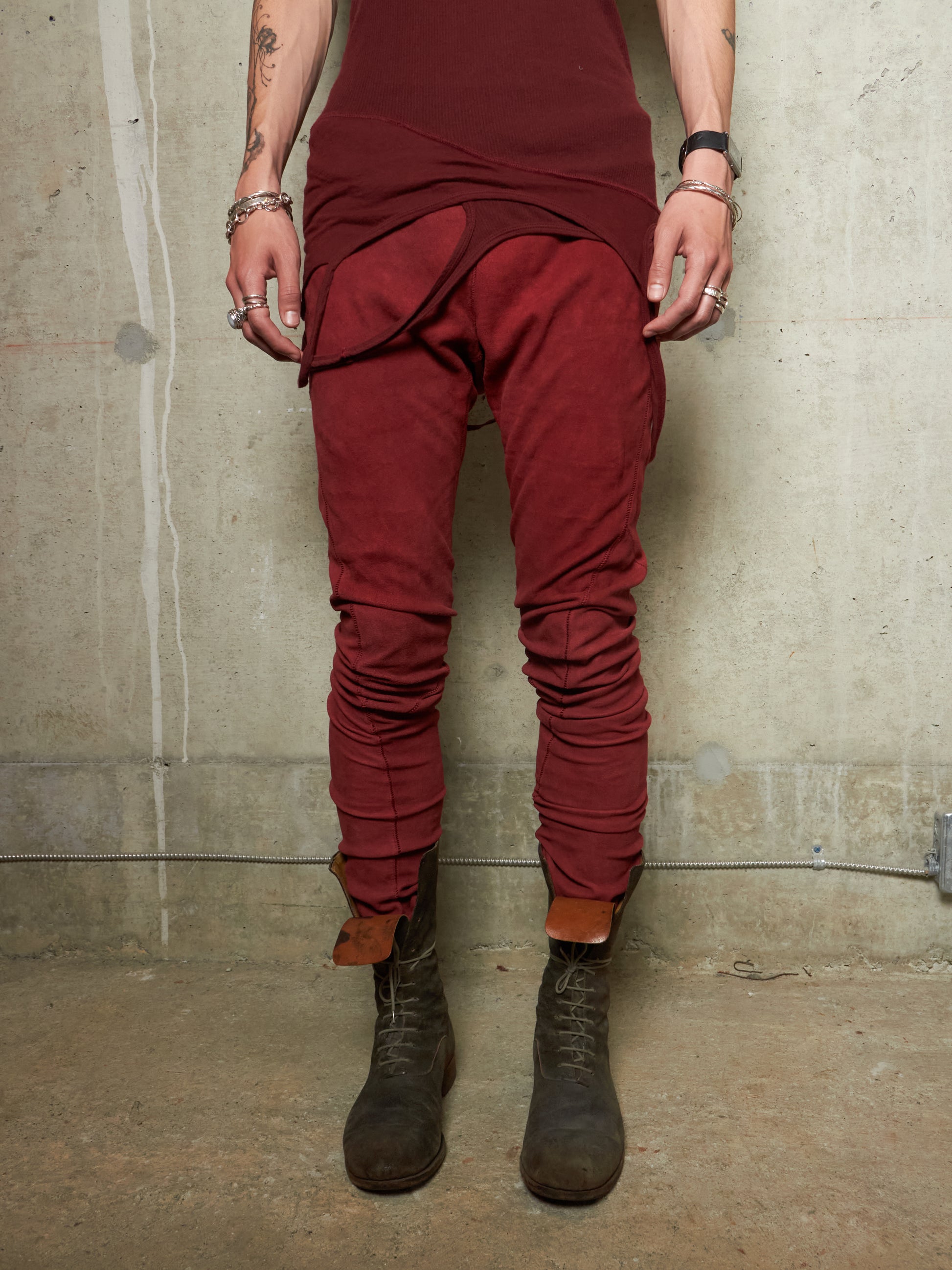 Person wearing a burgundy outfit with a tunic and pants, standing against a concrete wall.
