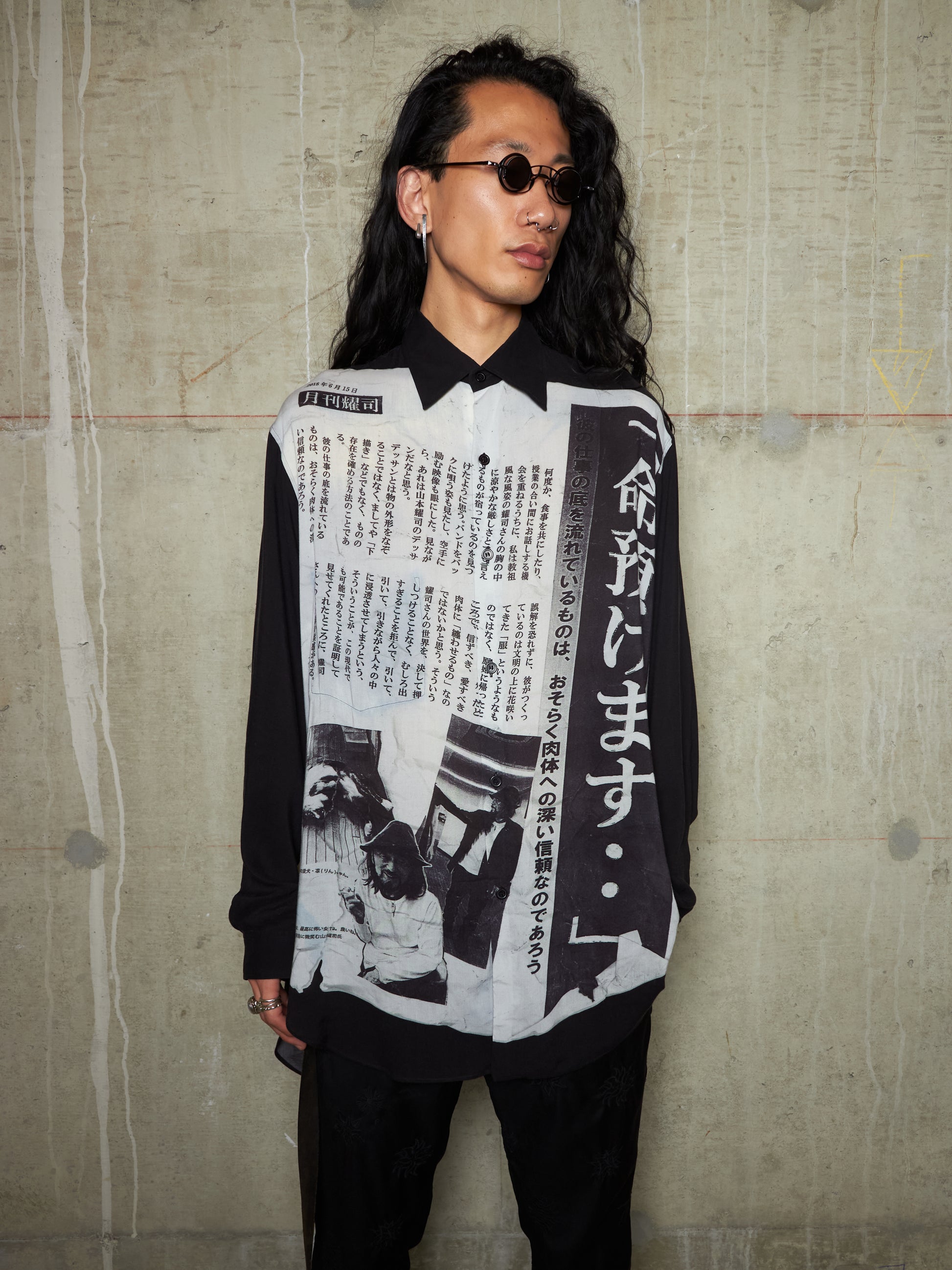 Person wearing a black and white patterned shirt with text against a textured wall.