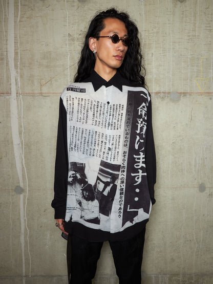 Person wearing a black and white patterned shirt with text against a textured wall.