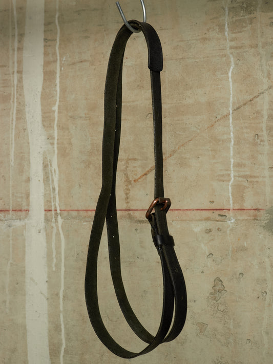 A dark leather strap, likely a reins or lead, hanging from a metal hook against a textured, distressed beige wall.
