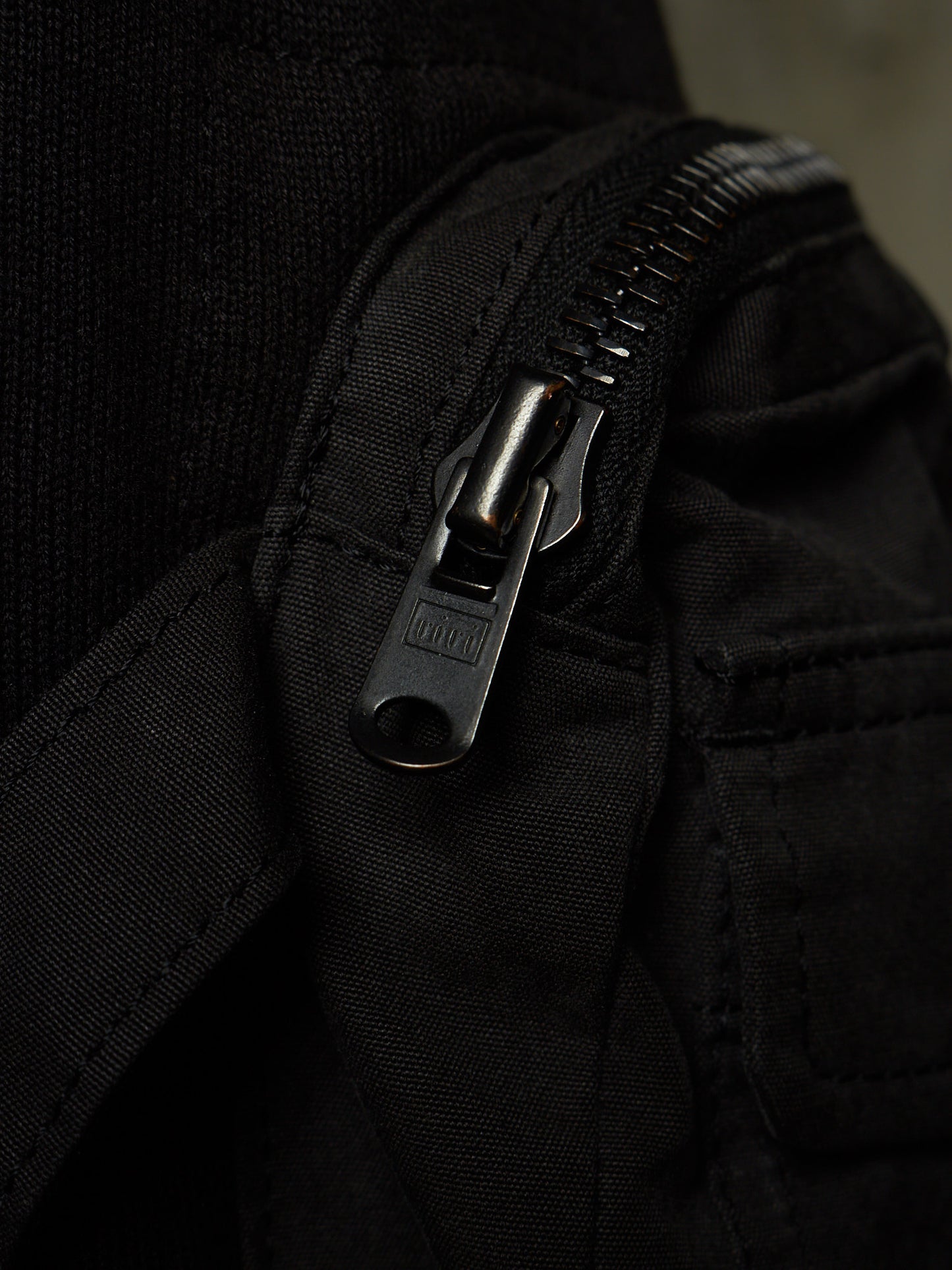 Close-up of a black fabric zipper with a dark metal pull tab on a black textile item.