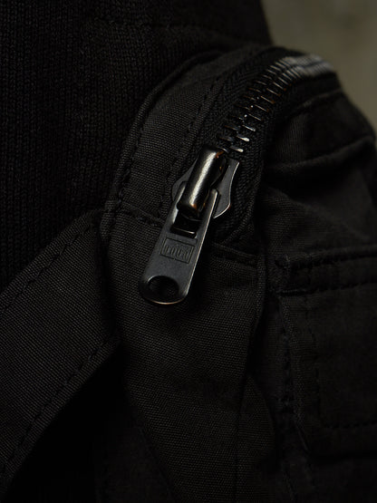 Close-up of a black fabric zipper with a dark metal pull tab on a black textile item.