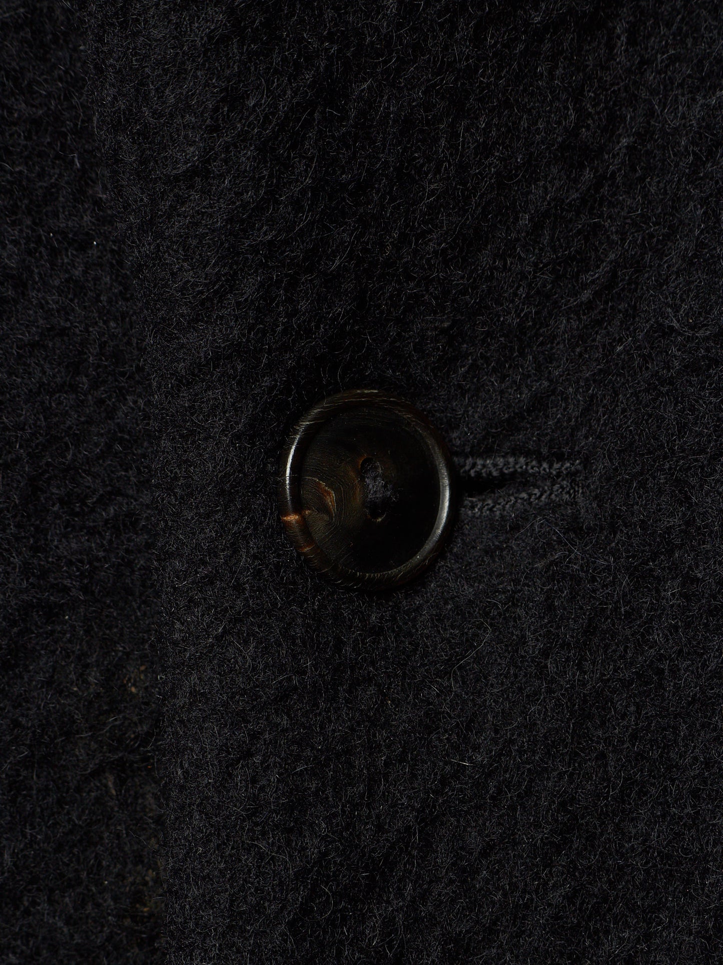 A close-up of a dark brown button on a textured black wool fabric.