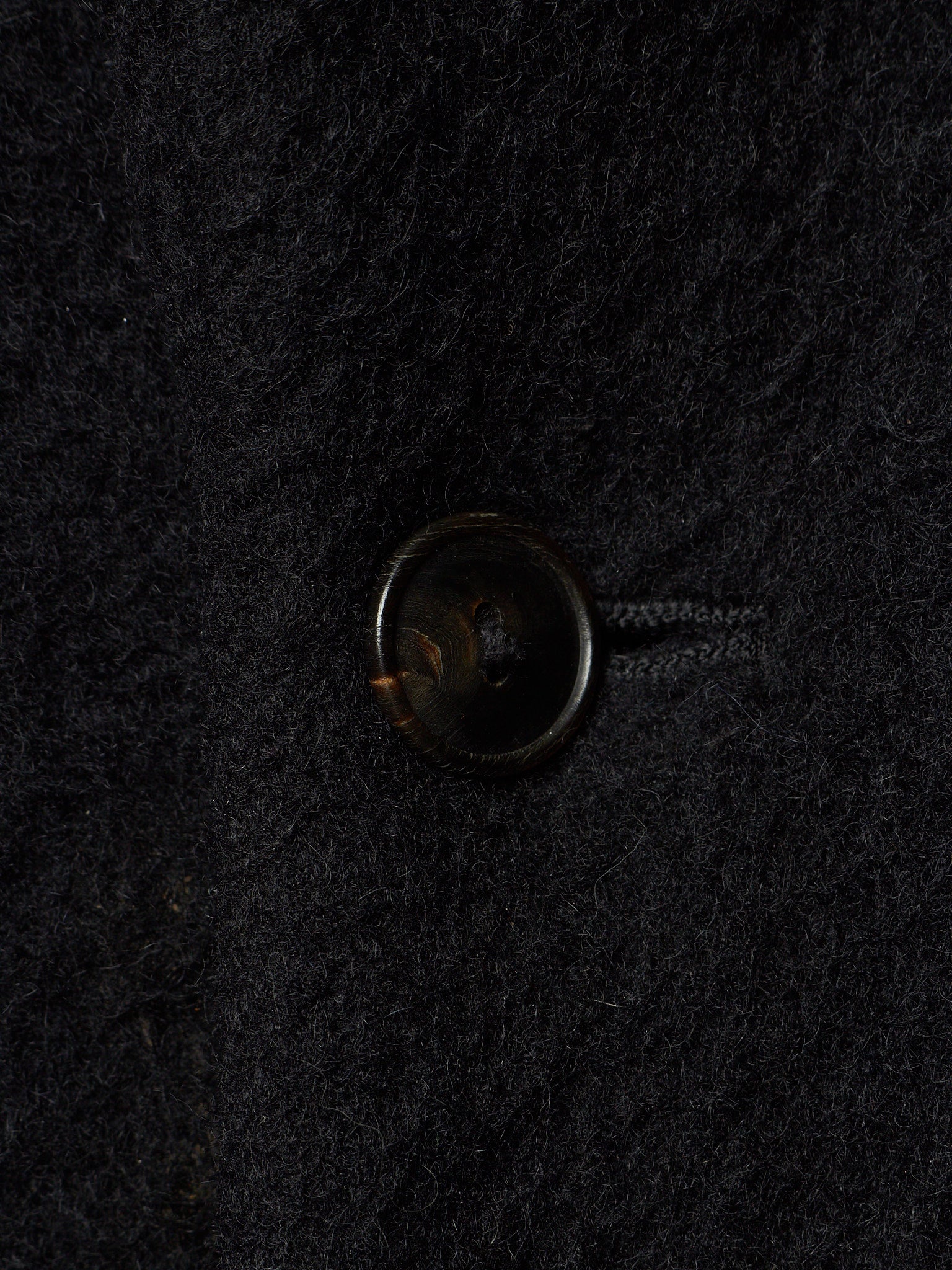 A close-up of a dark brown button on a textured black wool fabric.