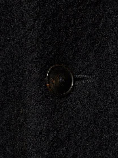 A close-up of a dark brown button on a textured black wool fabric.