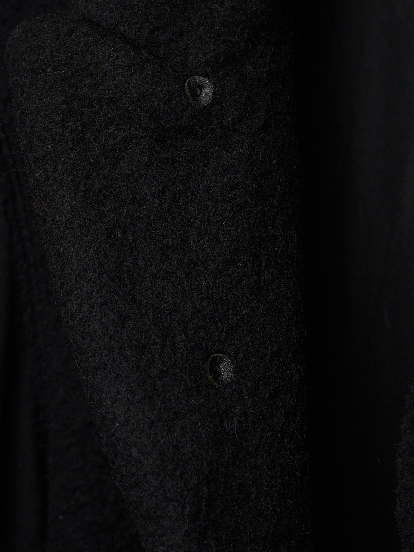 Close-up of a dark textured fabric garment with two visible buttons on a black background.