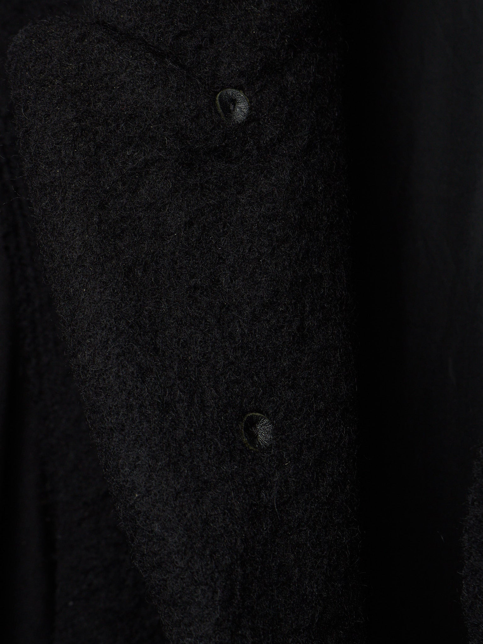 Close-up of a dark textured fabric garment with two visible buttons on a black background.