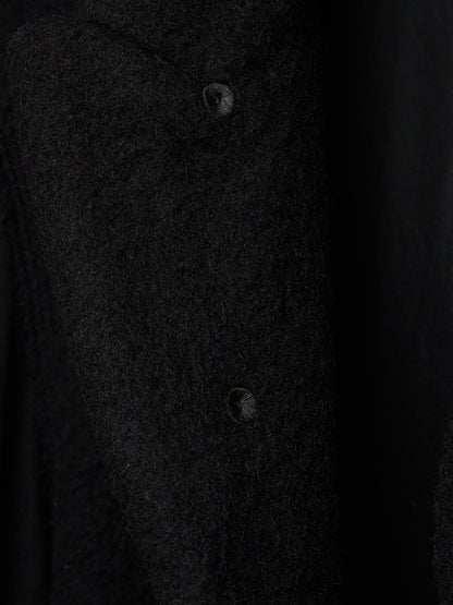 Close-up of a dark textured fabric garment with two visible buttons on a black background.