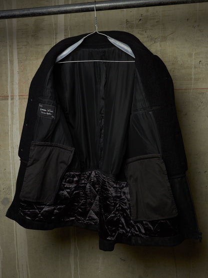 A black quilted jacket with a shiny black satin lining, hanging on a metal hanger against a textured concrete wall.
