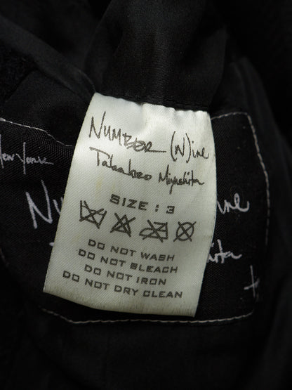 A close-up of a black garment's interior label, featuring a white rectangular tag with handwritten size information and care instructions. The handwritten text identifies the brand as 'Number (Wine) Takahiro Miyakita'.