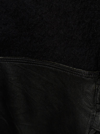 Close-up detail of a black garment showing a textured black fabric upper section and a black leather lower section with visible stitching.