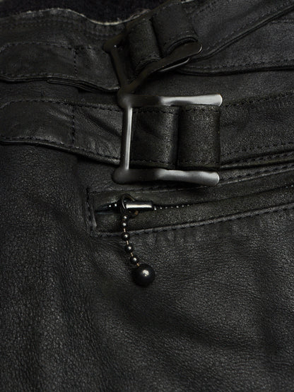 Close-up of black leather pants showing a belt buckle, belt strap, zipper pocket, and a small black bead chain detail.