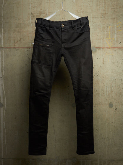 Black slim-fit jeans with zippered side pockets, hanging on a white wire hanger against a textured concrete wall.