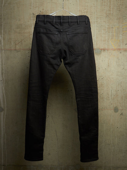 Black slim-fit jeans shown from the back, hanging on a clear plastic hanger against a textured concrete wall.