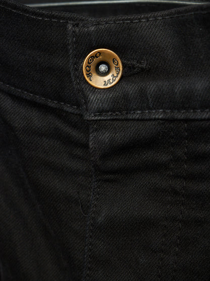 Close-up of black denim jeans showing the waistband and a round brass button with engraved branding.