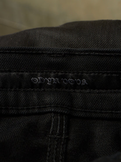Close-up of black denim fabric showing the embossed brand name 'ODYSSEUS' on the waistband.