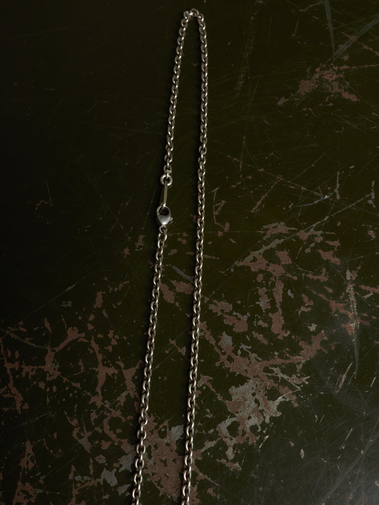 A silver-toned metal chain necklace with a small clear bead spacer, laid vertically on a dark distressed background.
