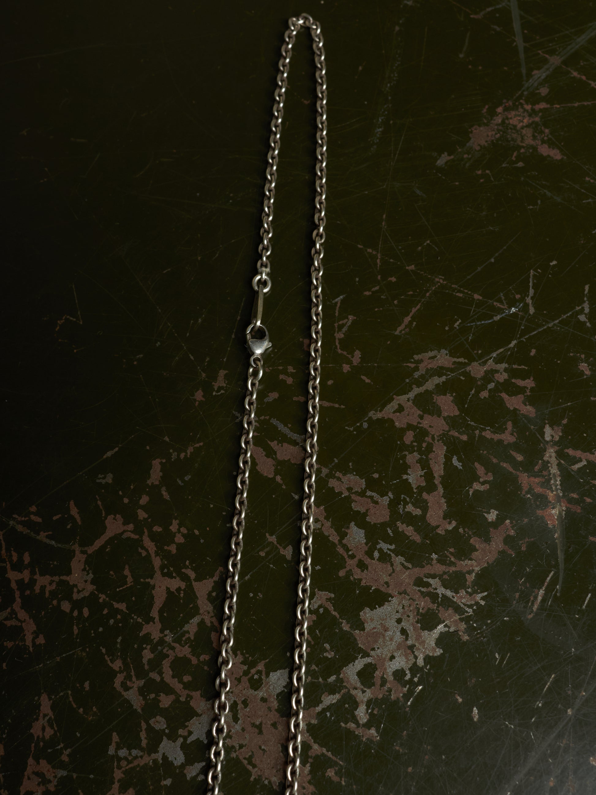 A silver-toned metal chain necklace with a small clear bead spacer, laid vertically on a dark distressed background.