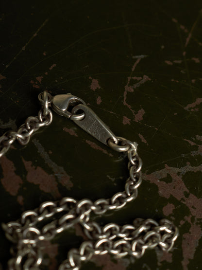 A close-up of a silver metal chain with a lobster clasp resting on a dark, distressed surface.