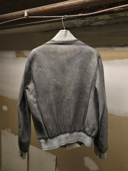 A gray washed suede jacket hanging on a white hanger against a rustic, unfinished wall with exposed pipes.