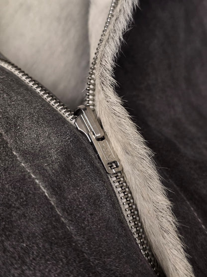 Close-up of a dark gray suede or shearling-lined jacket with a silver metal zipper and a light gray faux-fur trim.