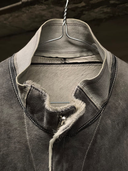 Close-up of a dark gray textured garment with a high collar, showing contrast stitching, raw frayed edges, and a light gray inner collar lining, hanging on a metal hanger.