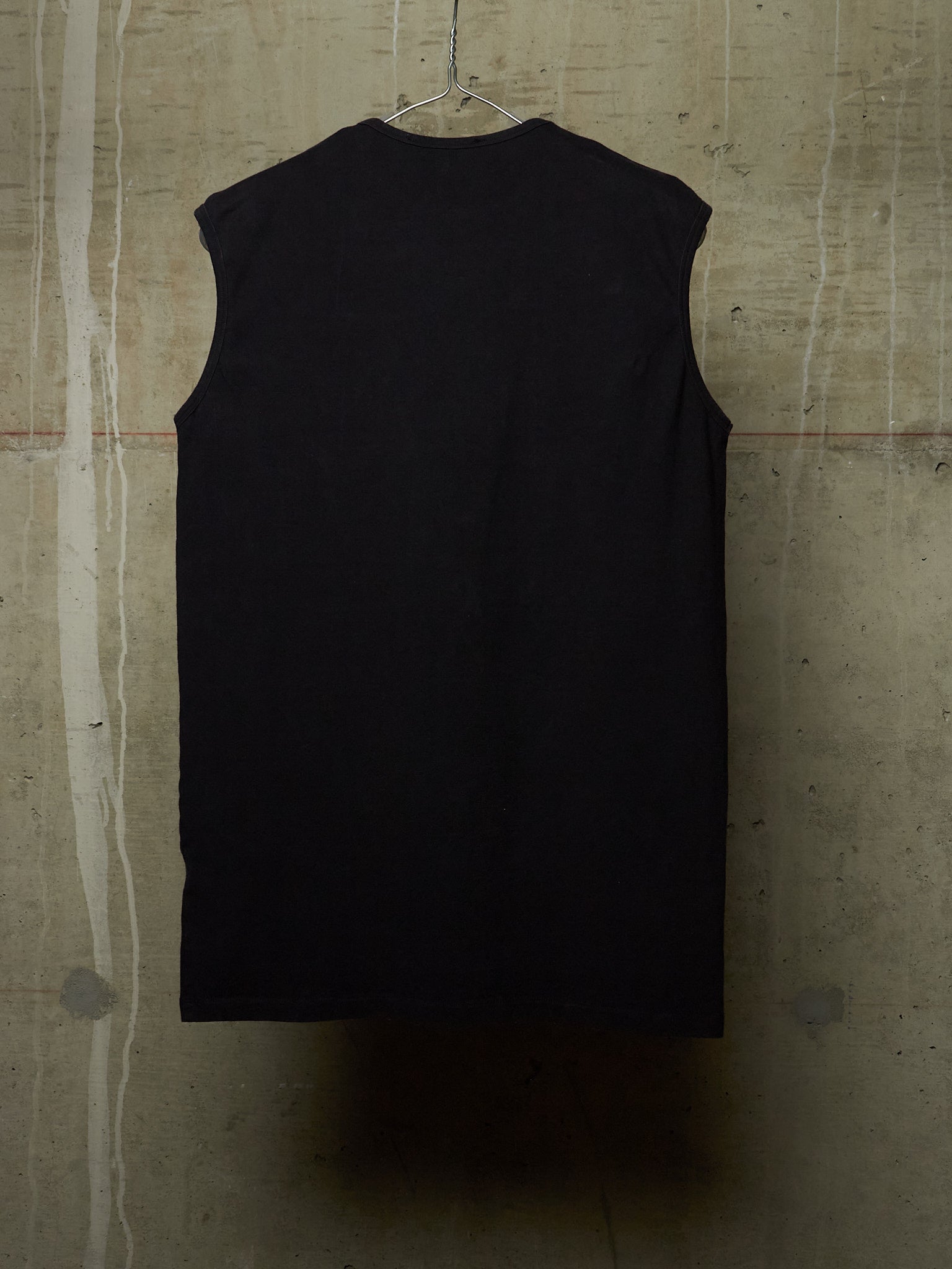 A black sleeveless top hanging on a wire hanger against a textured concrete wall.