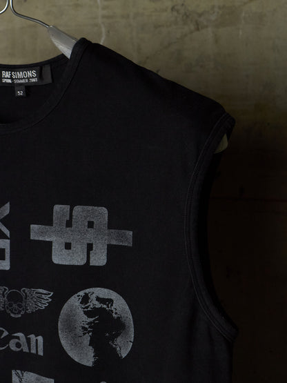 A black sleeveless tank top hanging on a metal hanger against a textured concrete wall. The shirt features a distressed gray graphic print with a stylized symbol, a winged emblem, and a globe design.