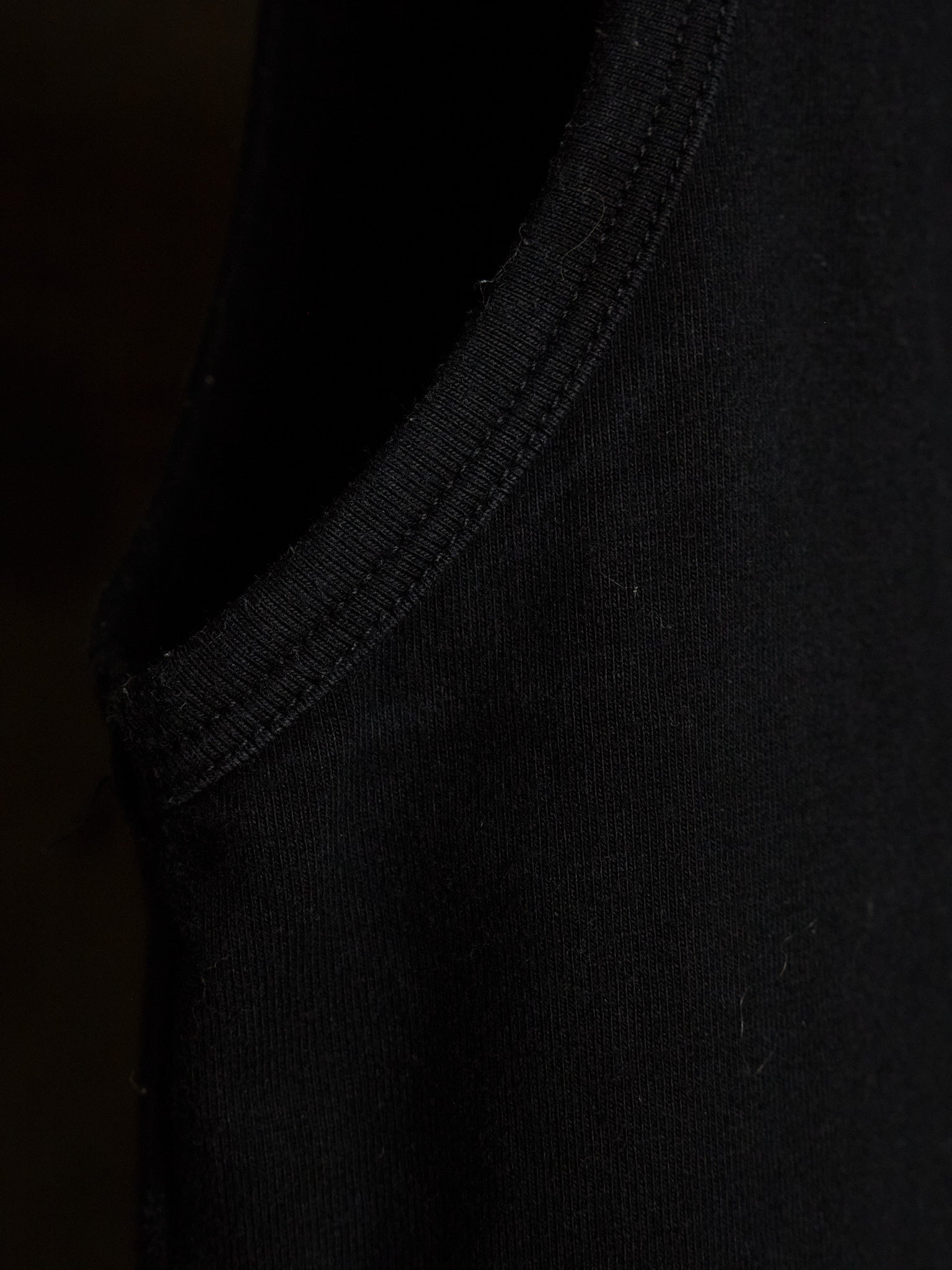Close-up detail of a black ribbed knit garment, showing the texture and stitching of the collar or sleeve edge.