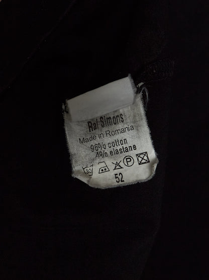 A close-up of a white fabric care label sewn onto a black garment. The label reads 'Rai Simons' and shows care instructions and the size number 52.