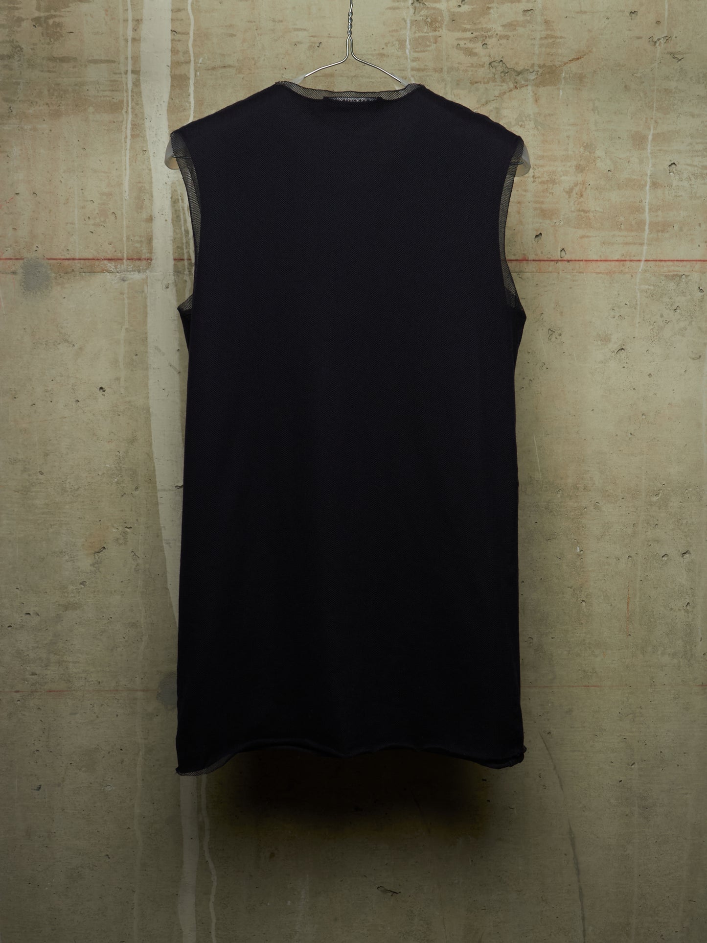 A sleeveless black top hanging on a metal hanger against a textured concrete wall.