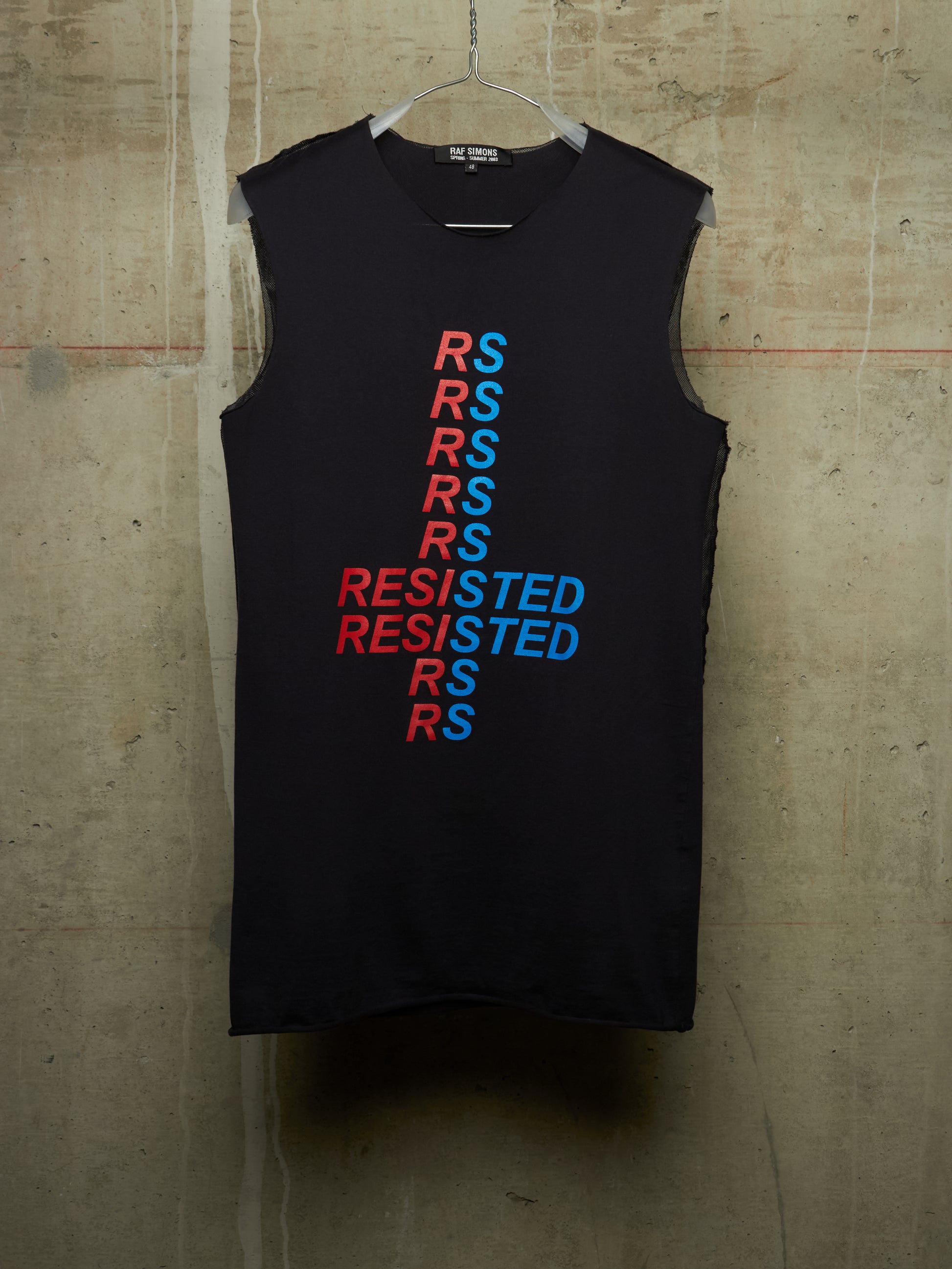 A sleeveless black tank top hanging on a wire hanger against a textured concrete wall. The front features a vertical graphic design spelling 'RESISTED' in alternating red and blue text.